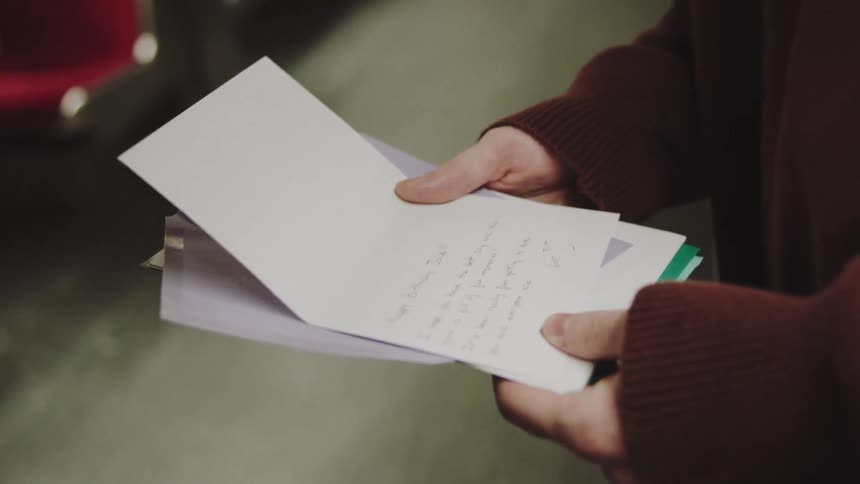The face of a young man holding some paper pamphlets and his hand he is inside a subway