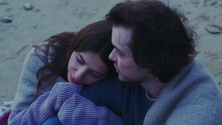 Woman resting her head on a mans shoulder while sitting on the beach sand