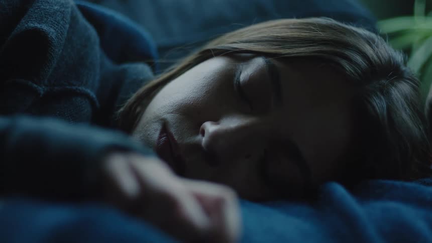 Young adult woman with a contemplative facial expression lying down against the chest of a young adult man on a couch indoors