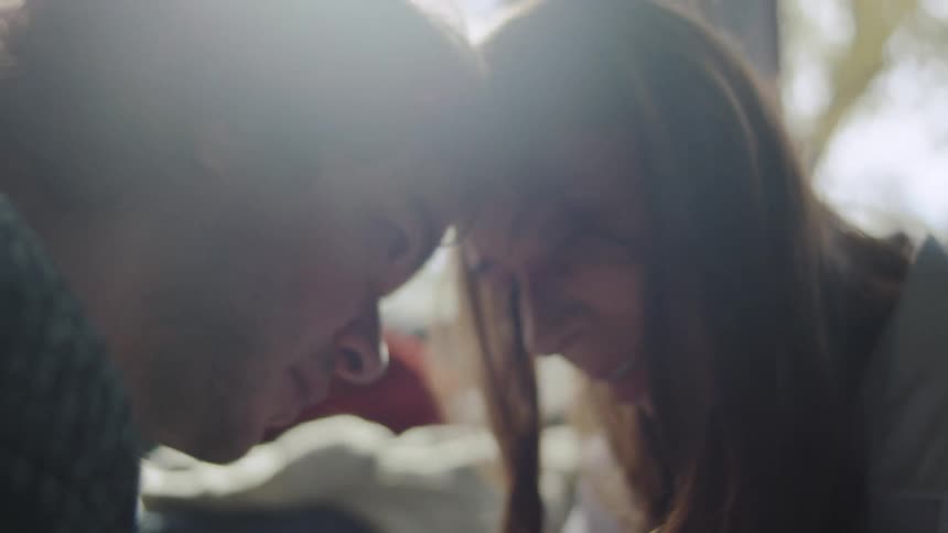 The video transitions from a closeup of a couples entwined hands to an intimate shot of their faces leaning together under strong backlight