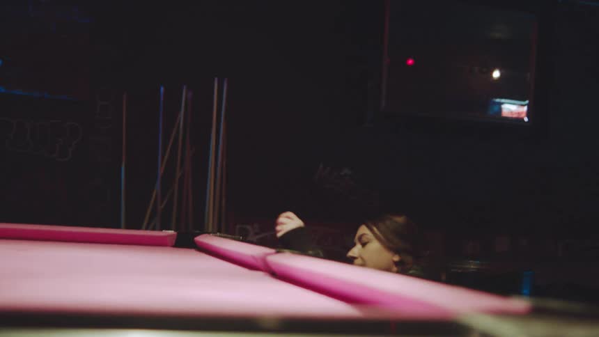 Young adult man talking to a young adult woman over a pool table at a bar indoors during night time