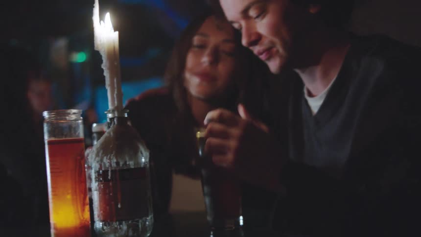 Couple sharing a drink at a table with a lit candle in a dimly lit indoor setting