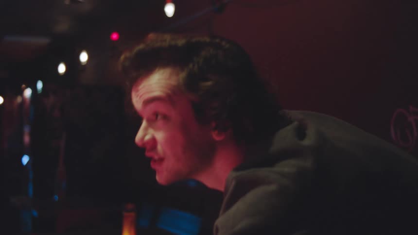 A young man holding a pool stick excitedly plays pool in a pub at night
