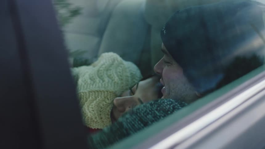 The man and woman are laughing and laying in the car