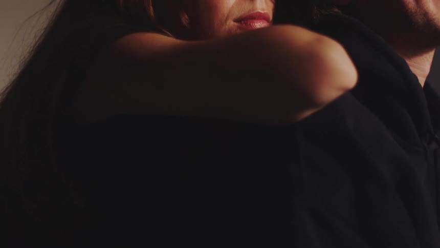 A close view of a woman with long hair resting her head on a mans dark clad shoulder in a dimly lit intimate indoor setting