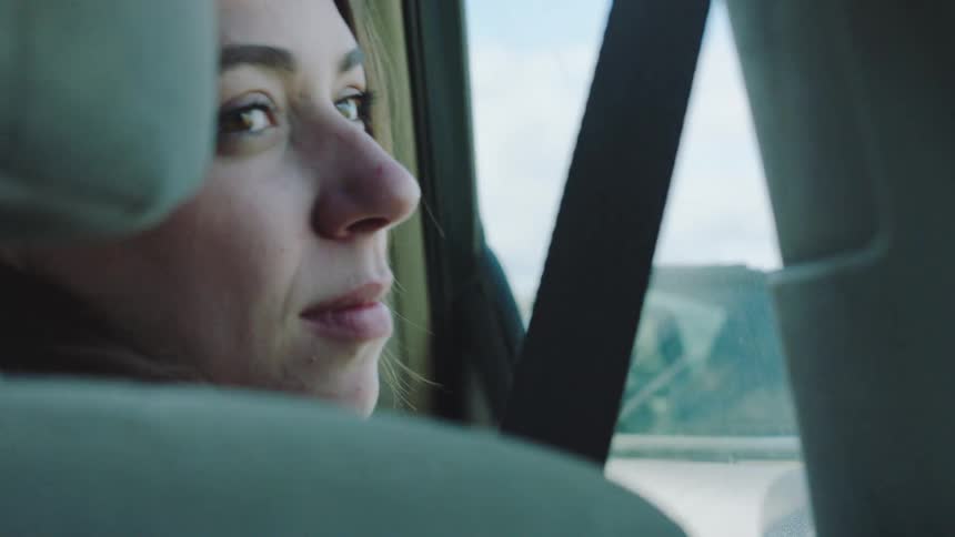 A woman riding in the backseat of a car looks out the window then smiles and points excitedly at something passing by