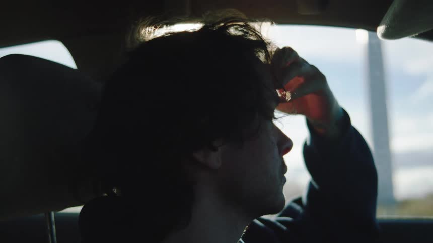 Man sitting in the car seat with his hand resting on his face while looking out the window