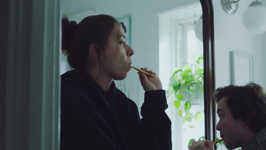 Young adult man and young adult woman brushing teeth in a bathroom indoors during day time