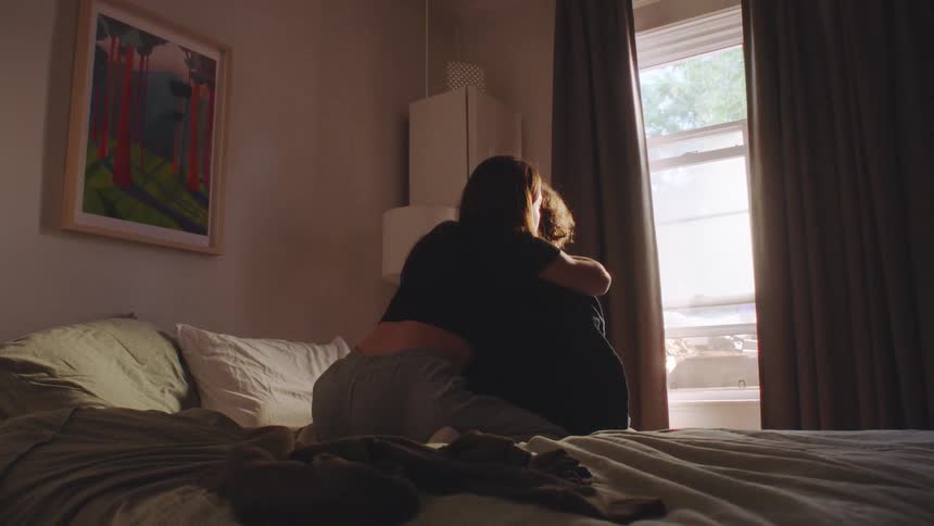Couple embraces on sunlit bed in cozy room with serene decor
