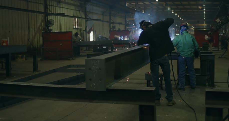 Welders work on a metal beam in a factory