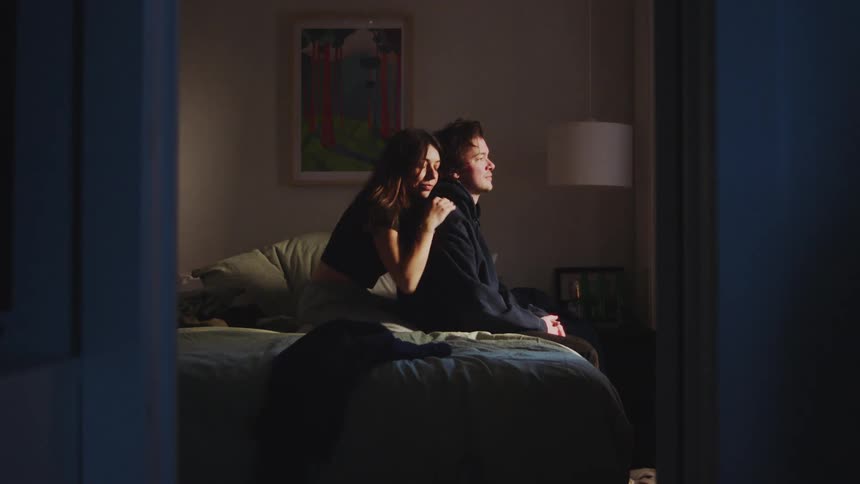 The woman hugs the man sitting on the bed