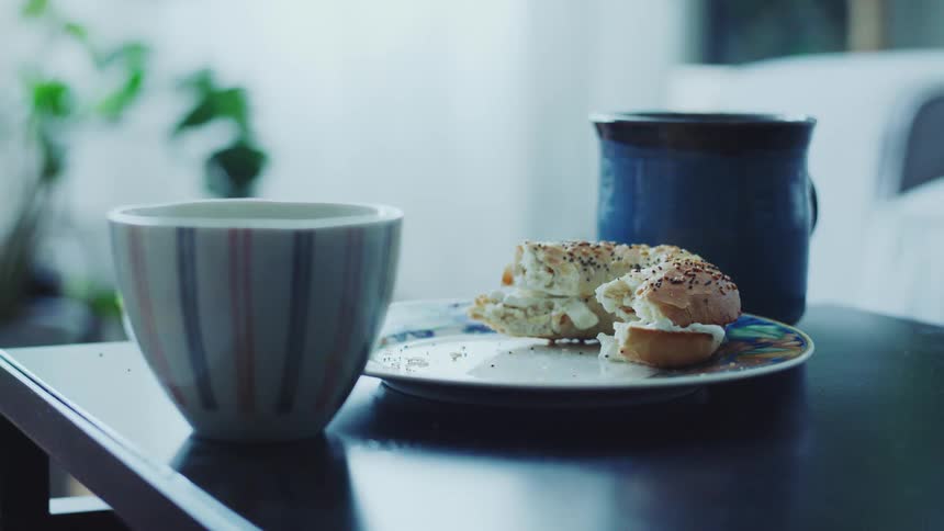 A bagel sandwich with a cup and mug on a table