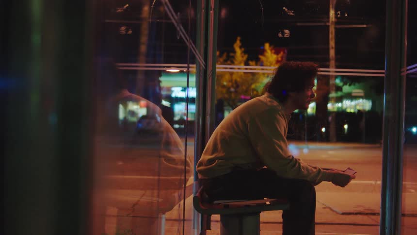 Man inserts a paper into an envelope while sitting at a bus stop at night