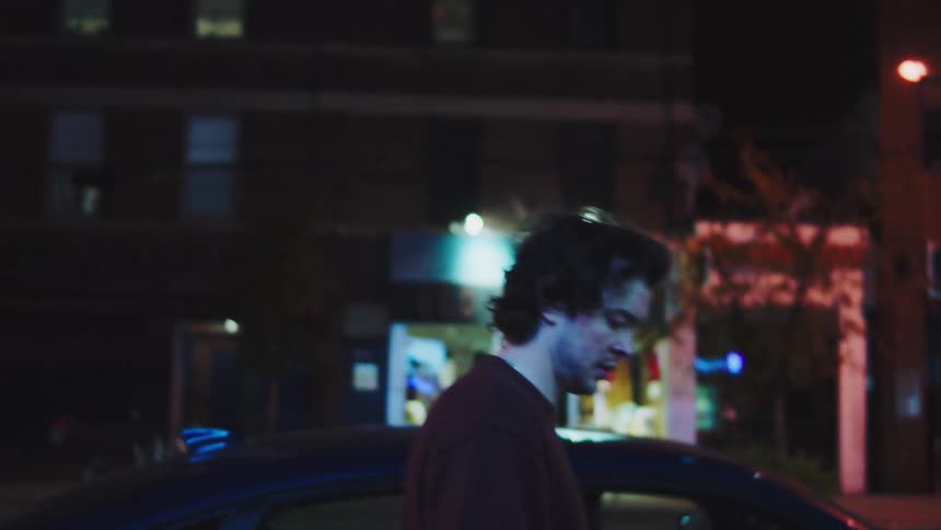 The man walks past the buildings at night
