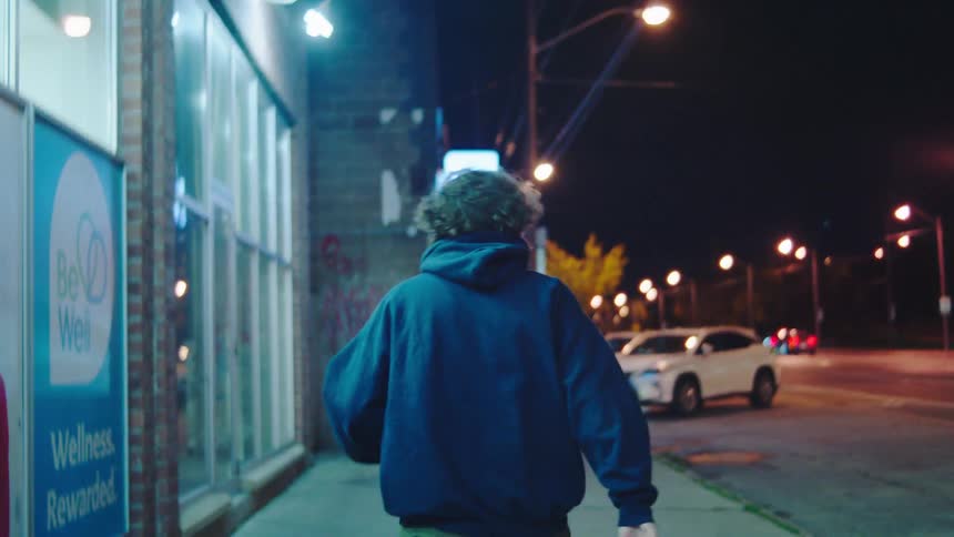 The man is walking on the sidewalk at night