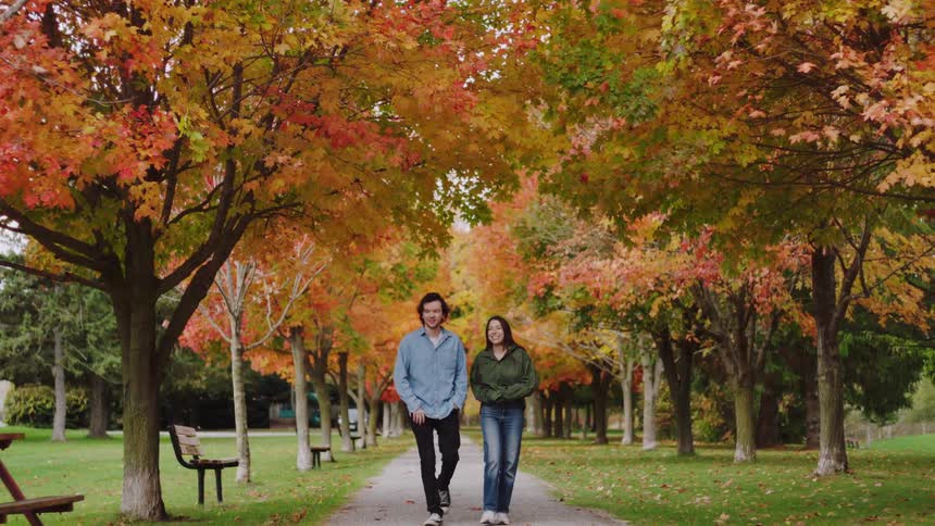 A couple walks together down a tree lined path covered in vibrant fall foliage