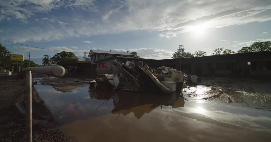 Debris with damaged furniture rests in flooded area outside motel under partly cloudy sky