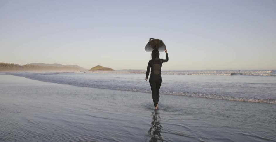 Woman walking into shallow ocean waves with surfboard on her head