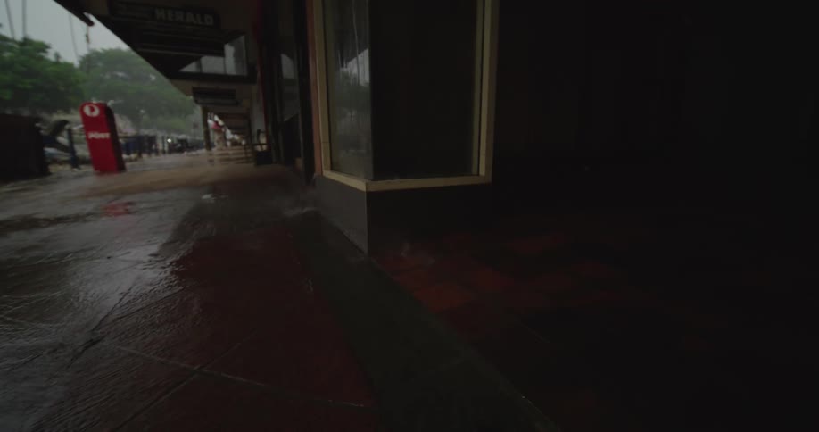 A walkway in the city at midday as rainwater gushes down from the roof