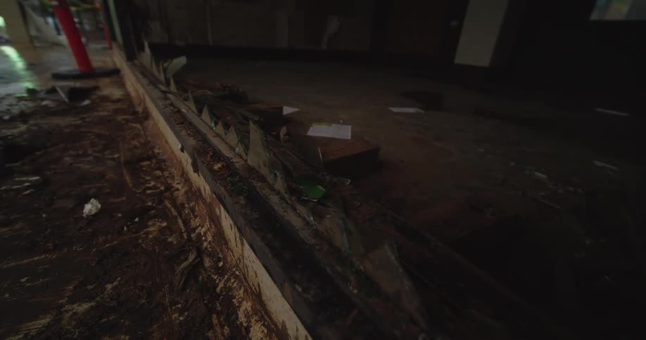 Abandoned indoor space with broken glass debris on floor and caution cone in dim setting
