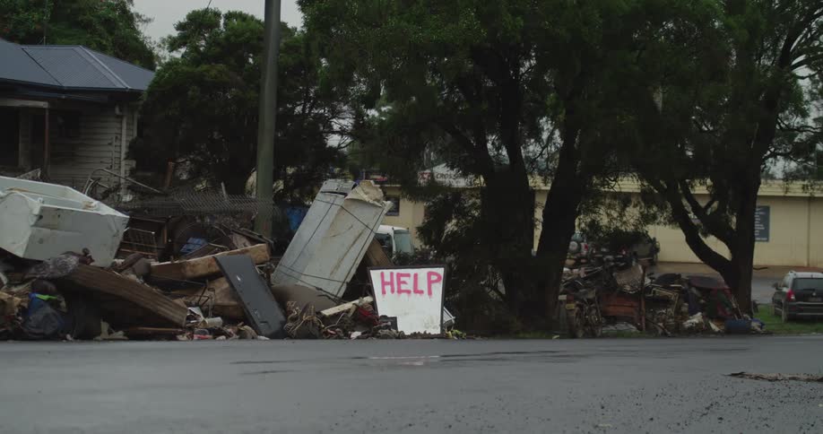 Cars drive past piles of trash and a sign that reads help