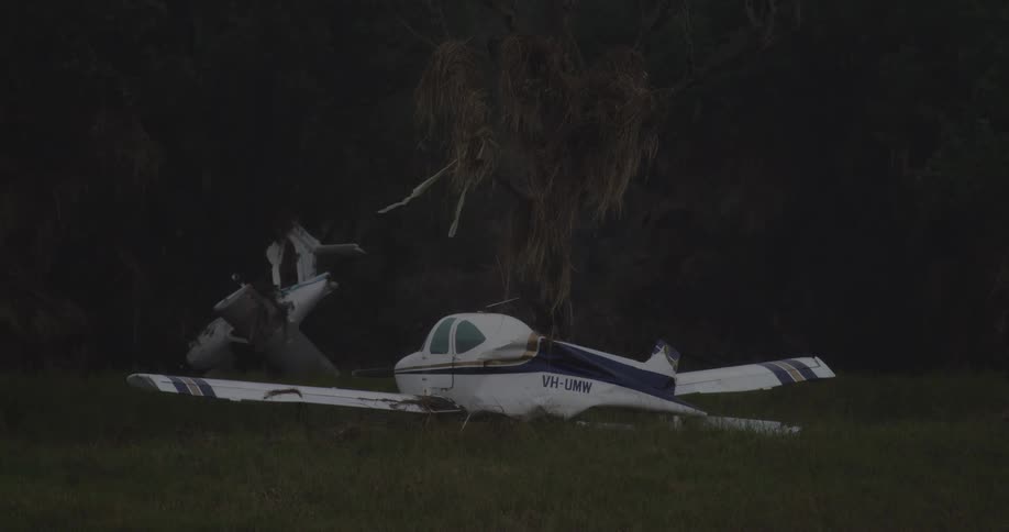 A crashed aircraft lies in a field at midday surrounded by scattered ruins