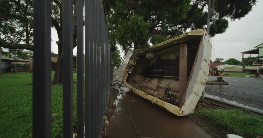 A boat lies on the side of the road beside a railing fence at midday