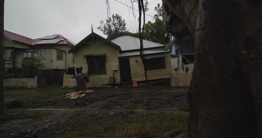 Yellow house leans on muddy ground surrounded by debris and loose planks