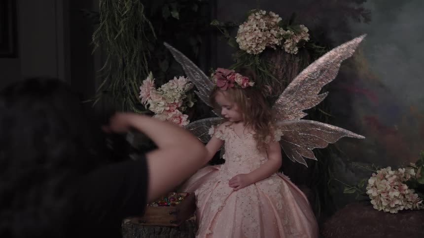 Girl dressed as a fairy sitting beside an open chest in a flowerdecorated studio