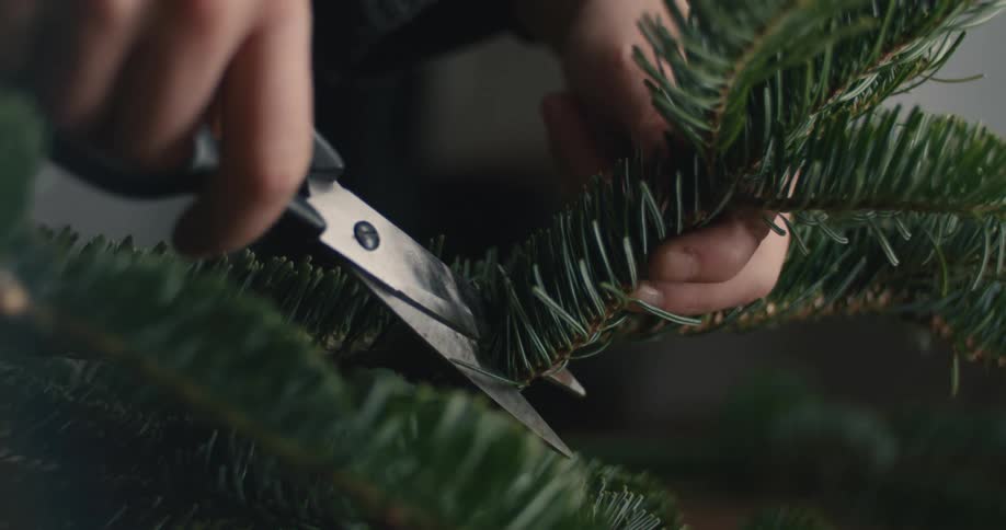 The woman cuts a branch on the wreath with scissors
