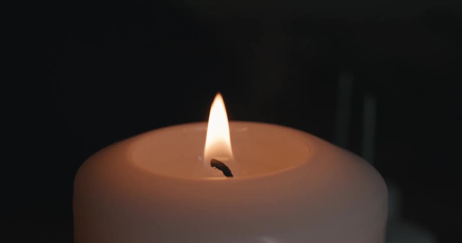 Close up of a person lighting a white candle in a room at night