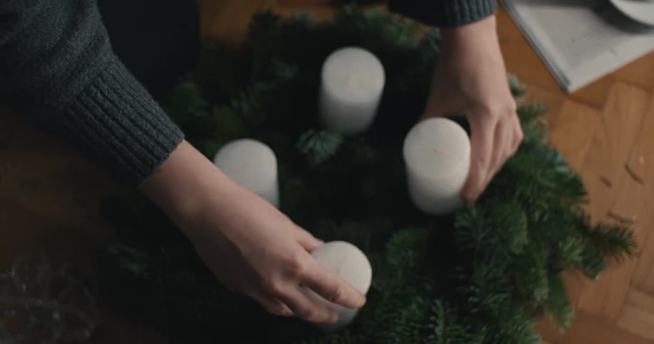 White candles are arranged in circular pine wreath on wooden floor