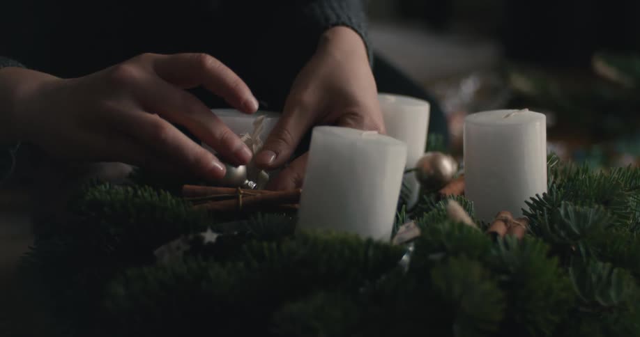 Hands arranging decorative items on festive wreath with candles cinnamon and holiday ornaments
