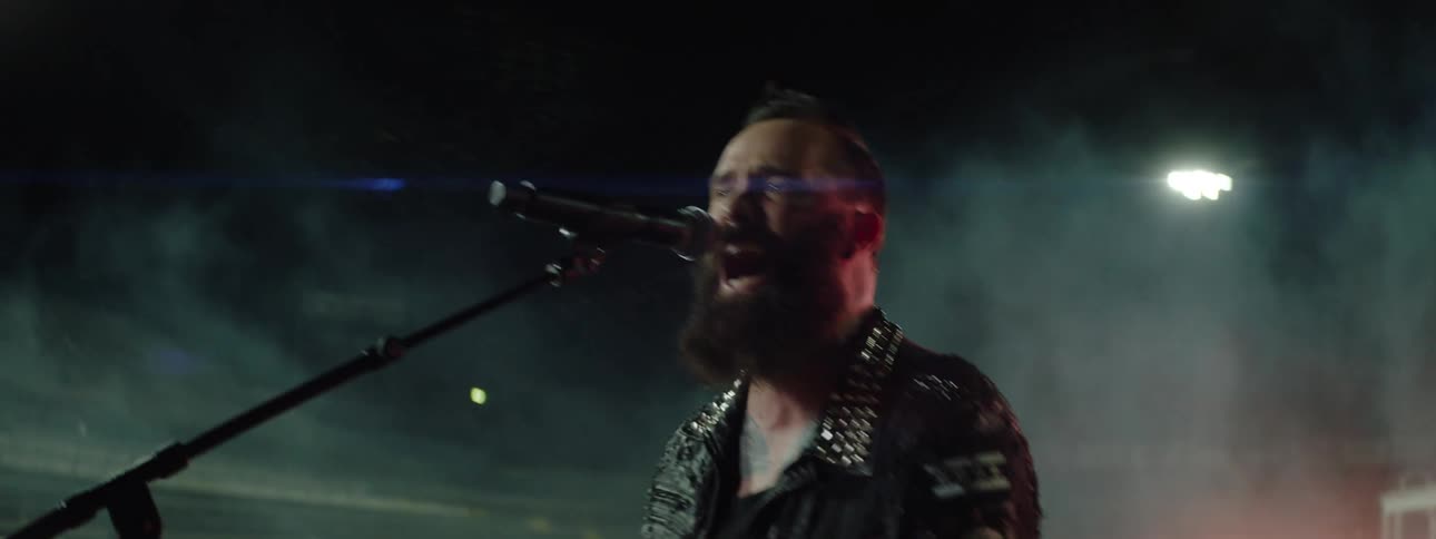 Singer in studded jacket performing on night stage with lights and smoke in background