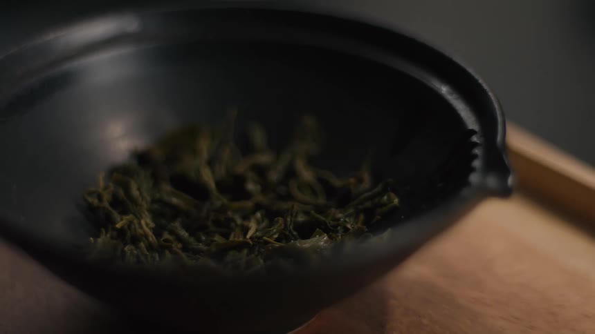 Dried green leaves in matte black bowl on wooden surface in soft natural composition