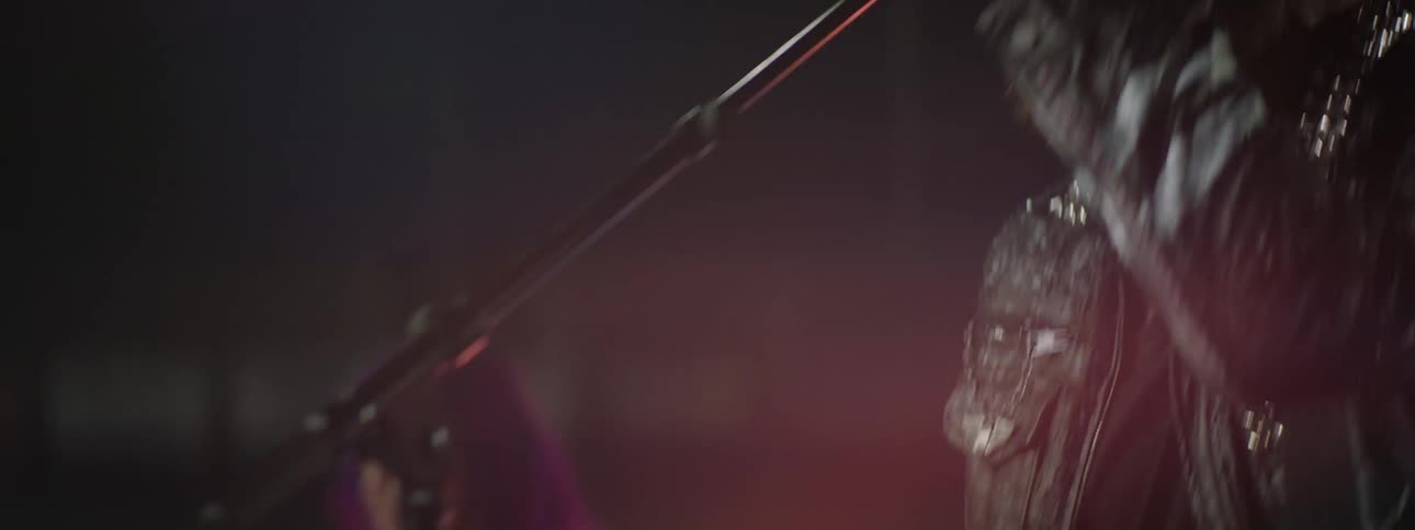 Bearded man singing into a microphone in a stage at a rock concert with a woman playing an instrument next to him indoors