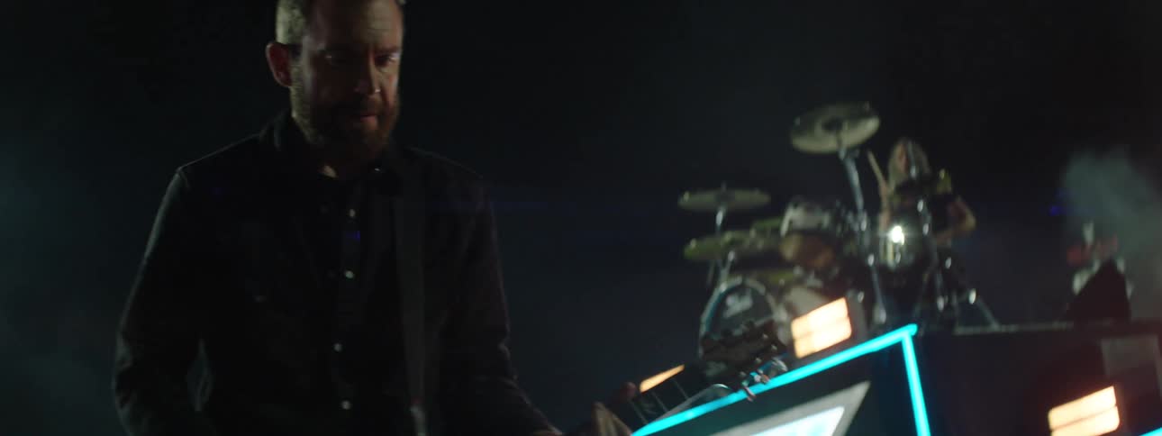 Person playing electric guitar with hands in focus under stage lights and illuminated panels in background