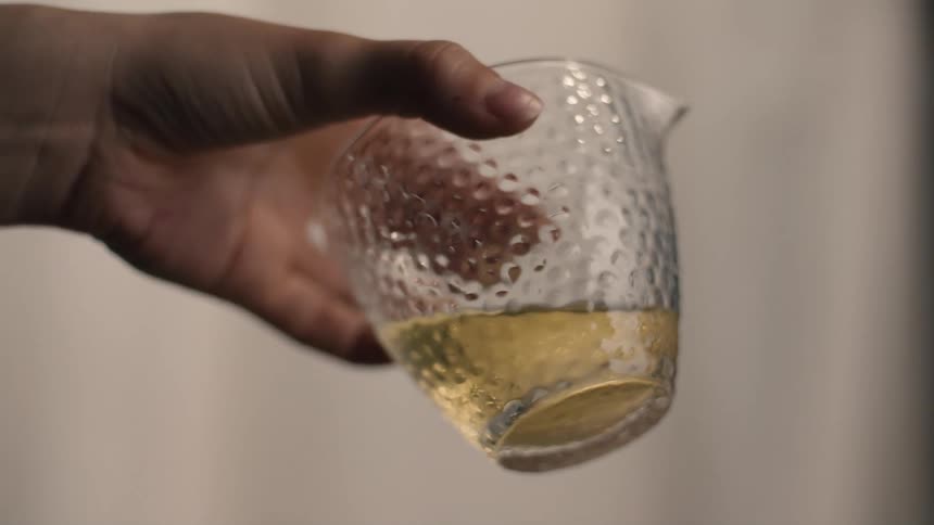 Yellowish liquid rests at bottom of textured glass container held by human hand
