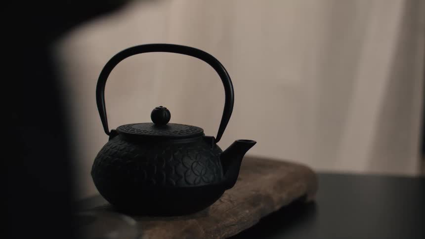 Black teapot with a handle covered by a lid on a wooden piece over a table indoors
