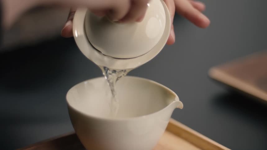 A woman pours tea into a cup placed on a wooden tray