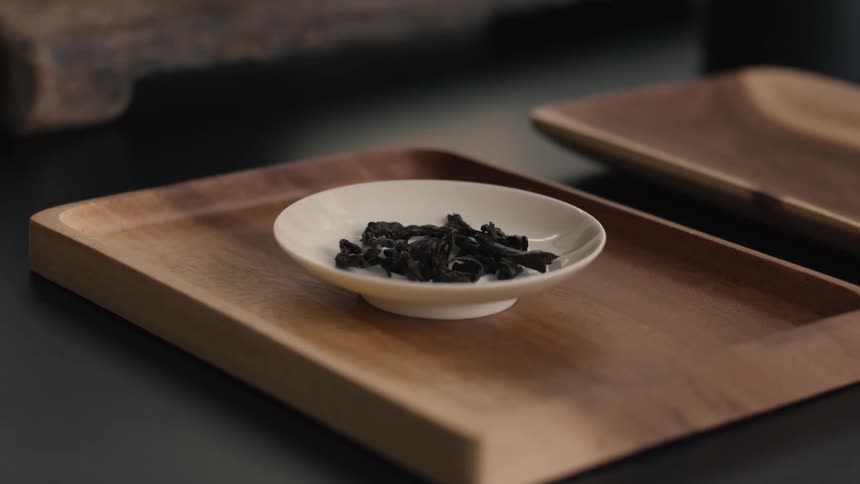 Dark tea leaves rest in white dish on wooden tray