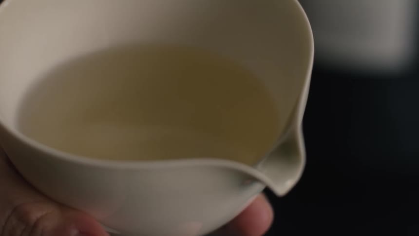 White cup with light tea being held by a hand in closeup
