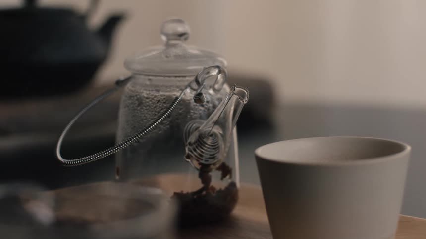 Metal infuser rests in glass jar with tea leaves beside white cup