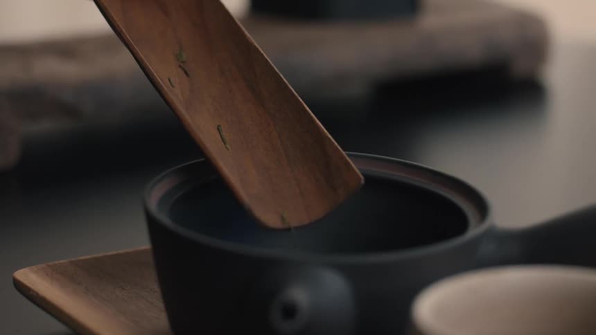 Close up of a person pouring tea leaves into a black kettle on a table
