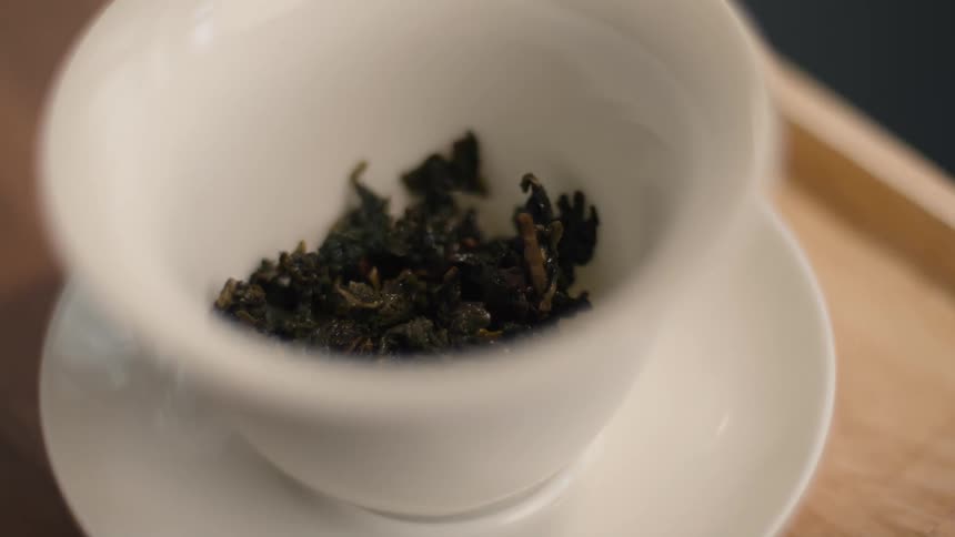 The white cup is on the white saucer holding tea leaves and on the wooden tray