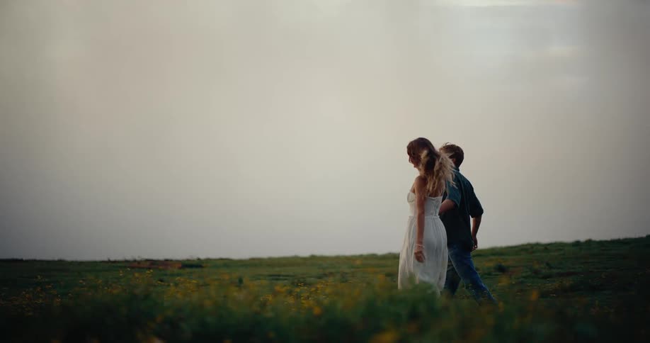 Couple walks through a field of wildflowers while holding hands on an overcast summer day