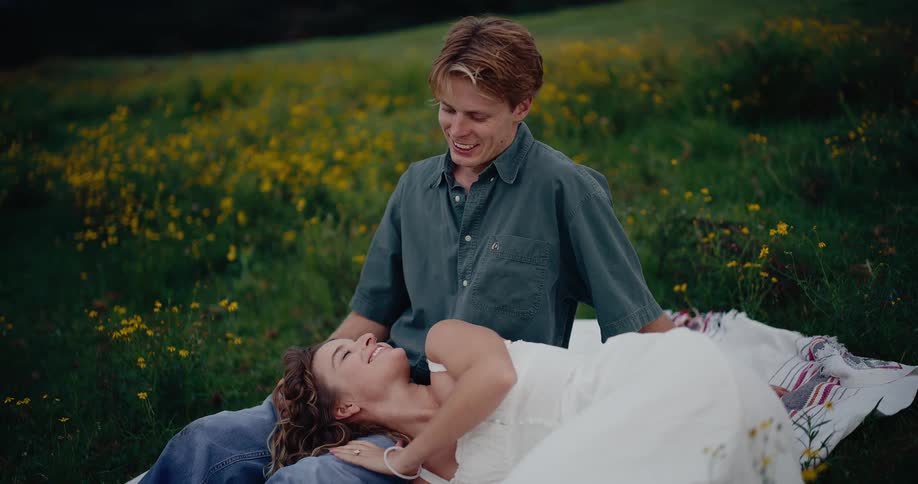 The woman is laying with her head on the mans lap while they are in a field of yellow flowers