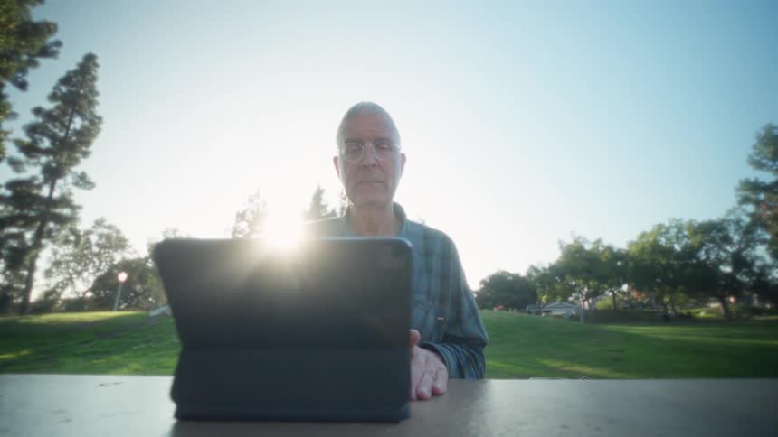 Man sitting outside at a table typing on a laptop computer keyboard