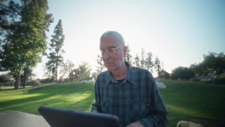 Man sitting outside at a table typing on a laptop computer