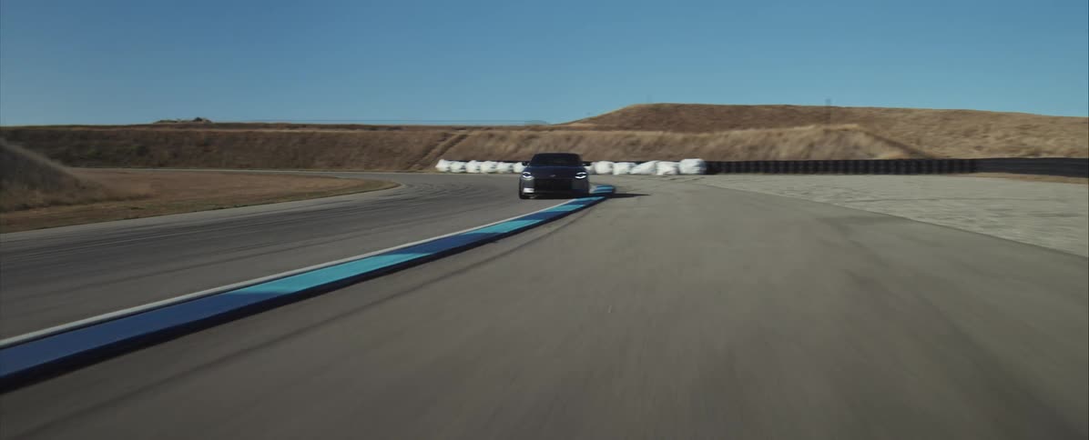 Dark sports car cornering on racetrack with headlights on under clear sky